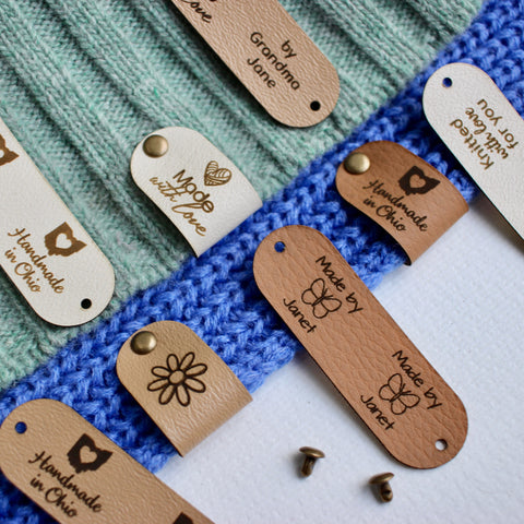 Multiple tags attached to knitted and crocheted fabric with custom logo, text and personalization in different shades, Attached with metal studs, also know as rivets in color bronze.